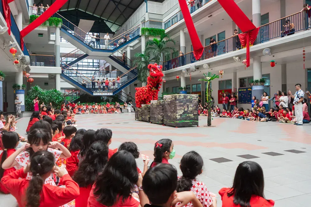 A group of children are sitting on the floor in a large building watching a performance.