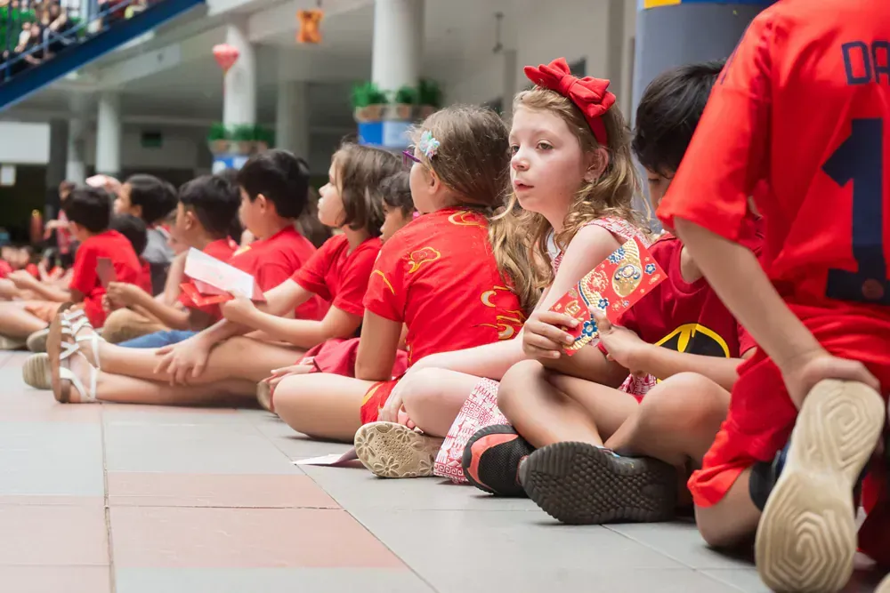 Children dressed in red, sitting on the floor during a school event, celebrating the Year of the Snake.