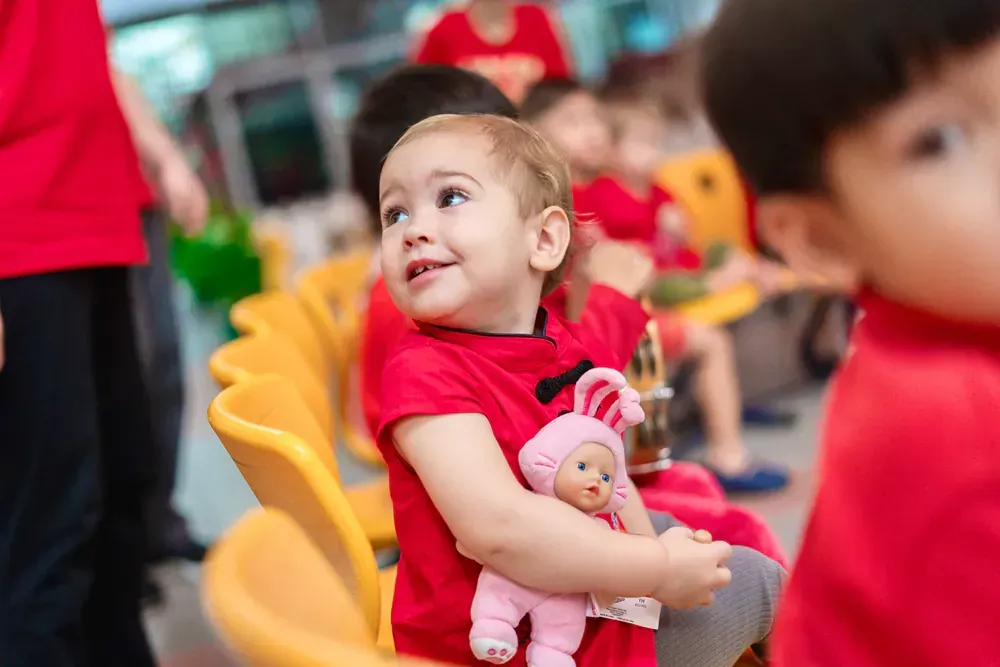 A little girl is sitting in a chair holding a pink doll.