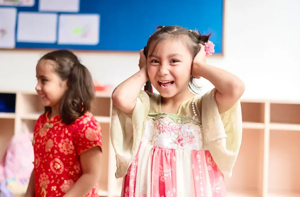 Two little girls are covering their ears in a classroom.