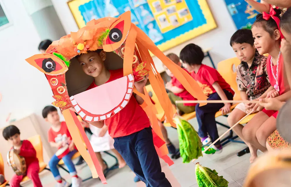 A group of children are playing with a lion head made out of paper.