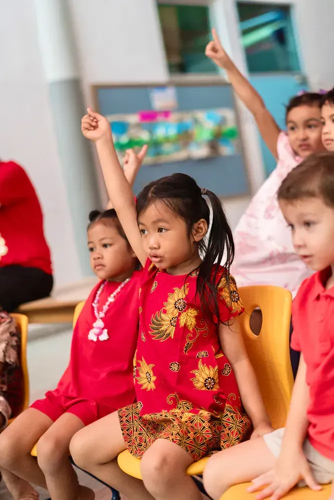 A group of children are sitting in chairs with their hands in the air.