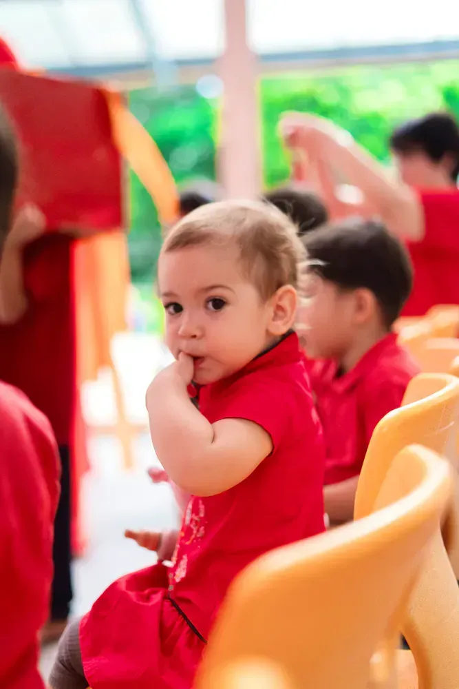 A baby in a red dress is sitting in a row of yellow chairs.
