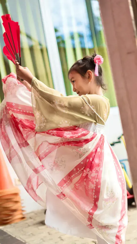 A little girl in a kimono is dancing with a fan.