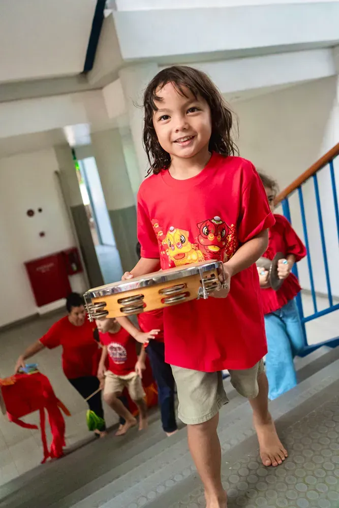 A young boy in a red shirt is holding a tambourine.