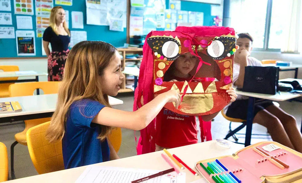 A young girl is sitting at a table in a classroom holding a puppet.