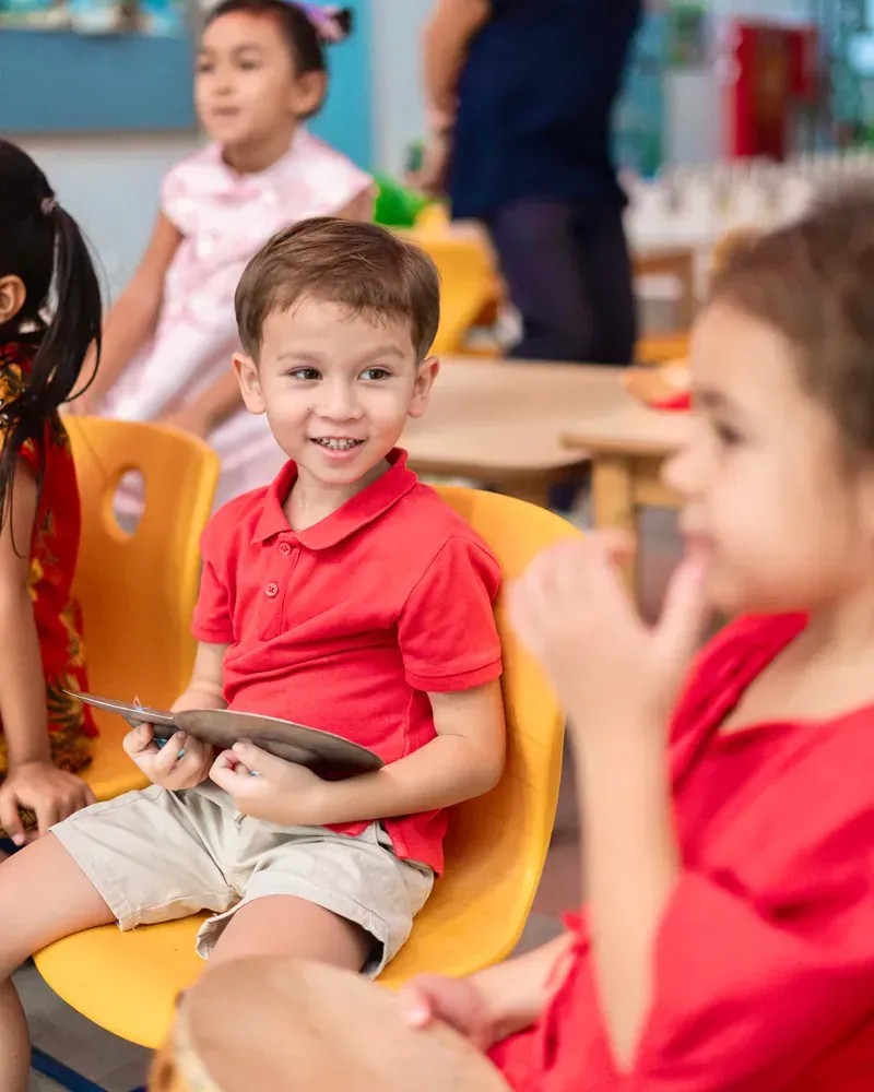 A group of children are sitting in yellow chairs in a classroom.