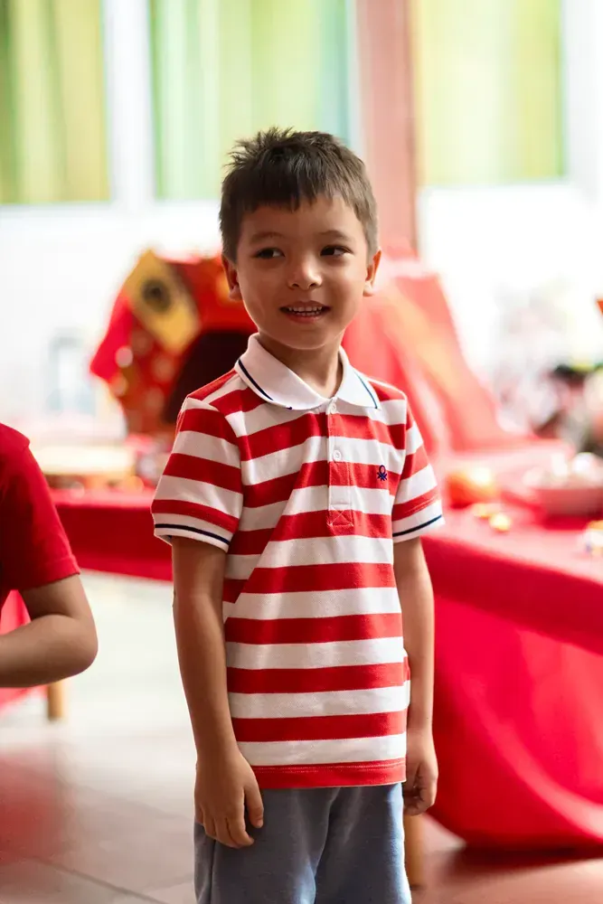 A young boy wearing a red and white striped shirt is standing in a room.