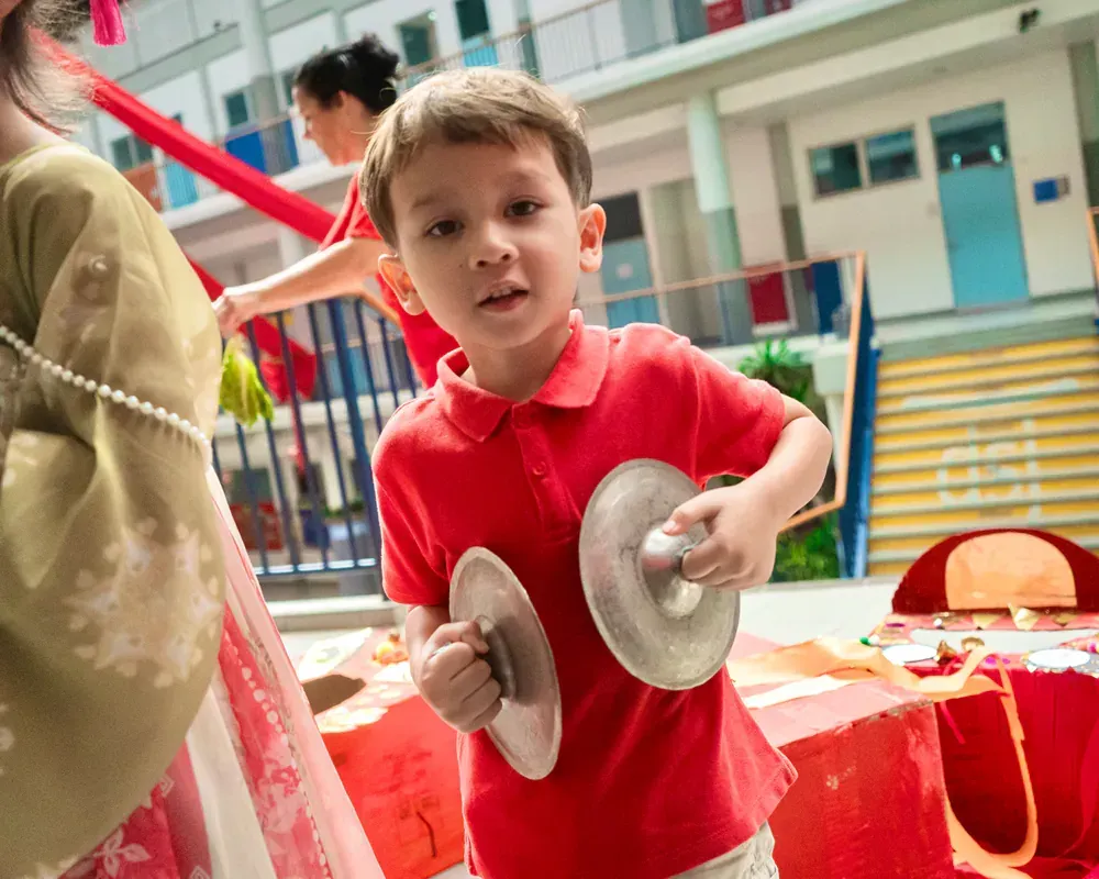 A young boy in a red shirt is holding a pair of cymbals.