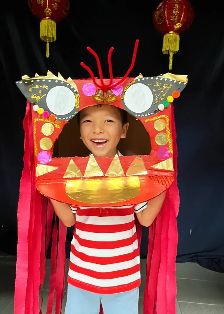 A young boy is wearing a cardboard dragon head
