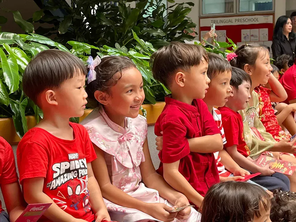 A group of children are sitting in a row wearing red shirts.