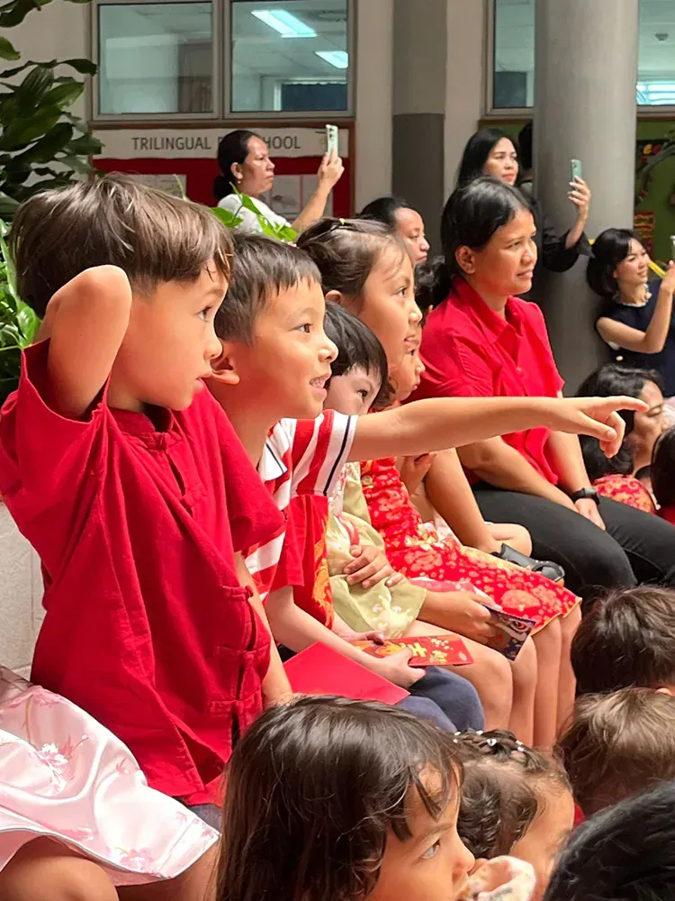 A group of children are sitting in a row and one of them is pointing at something.