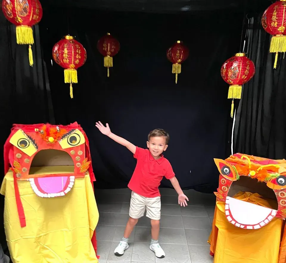 A young boy in a red shirt stands in front of chinese lanterns