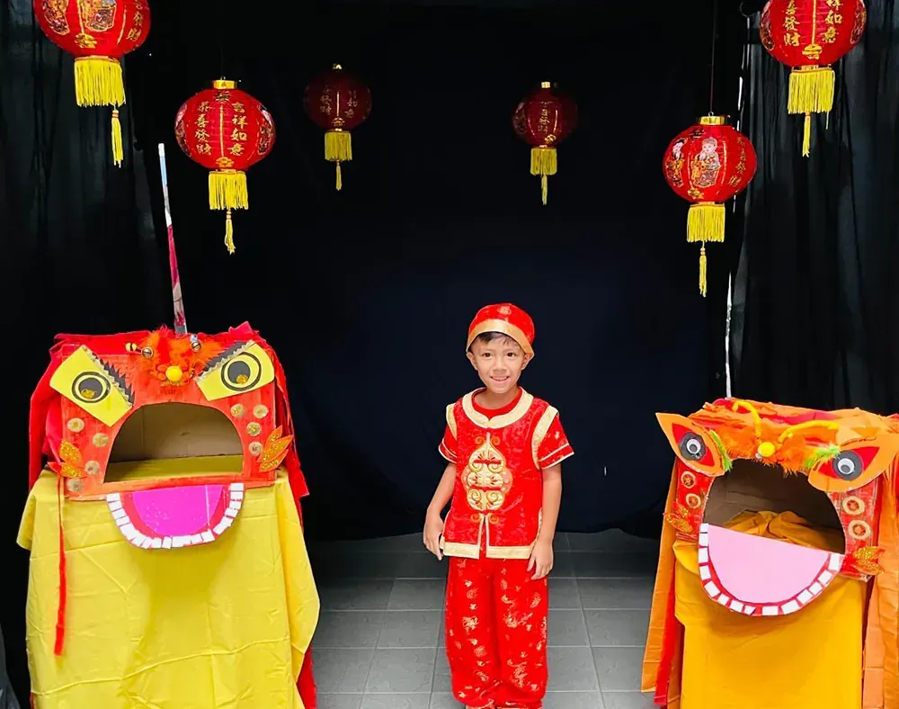 A young boy in a costume is standing in front of a lion head.