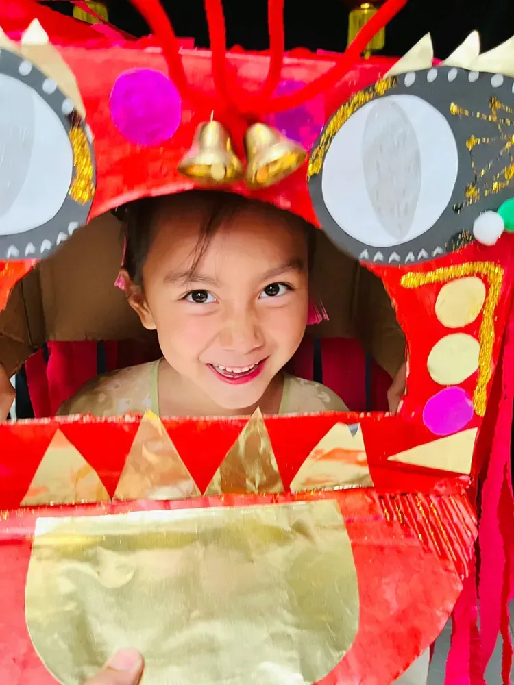 A smiling child inside a colorful handcrafted dragon costume, celebrating the Year of the Snake with traditional decorations.