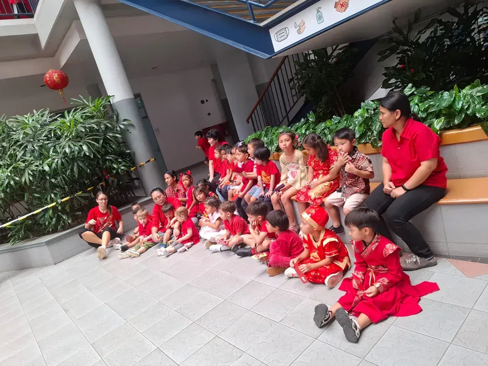 A group of children are sitting on the ground in front of a building