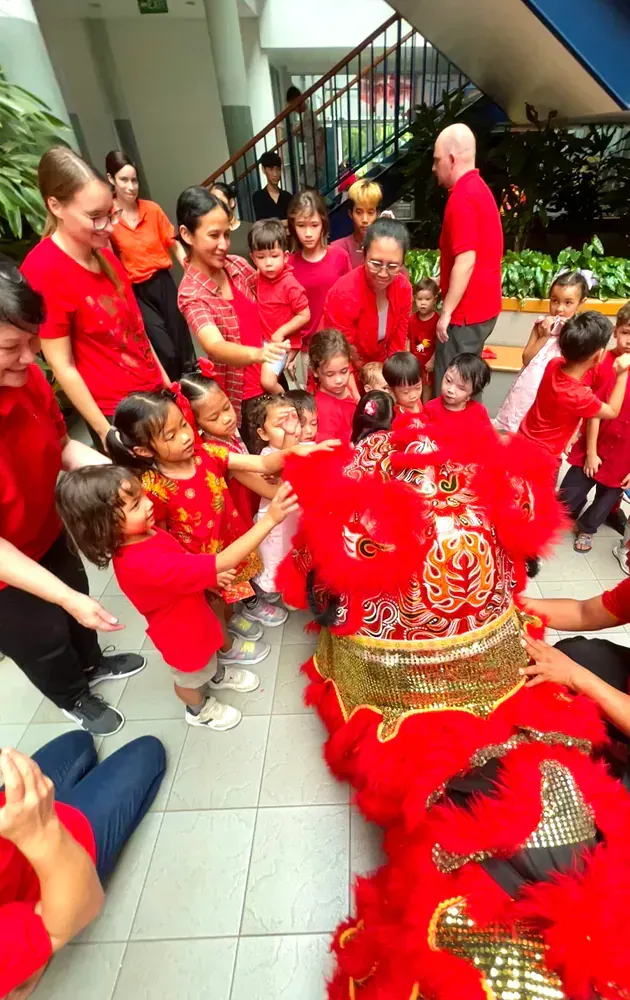 A group of people in red shirts are standing around a lion costume.
