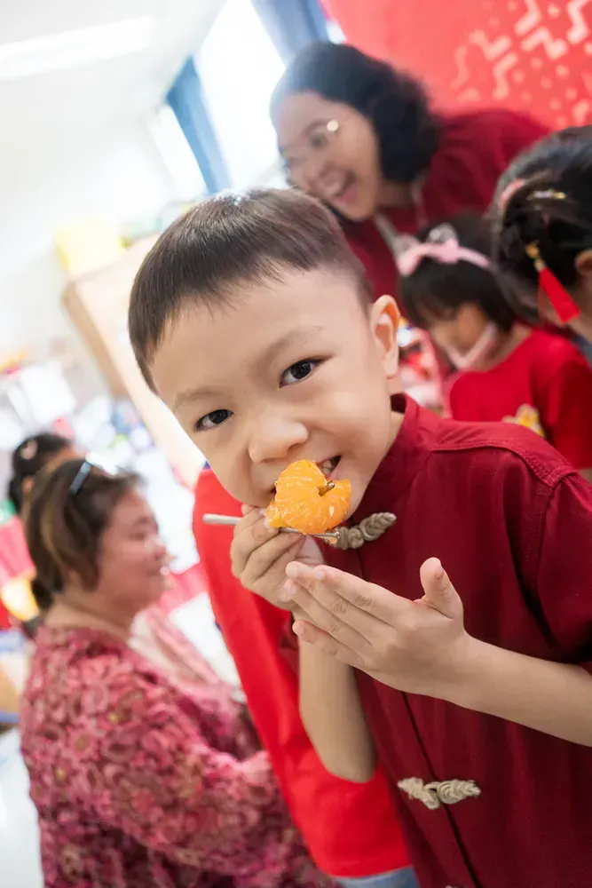 A young boy in a red shirt is eating a piece of food.