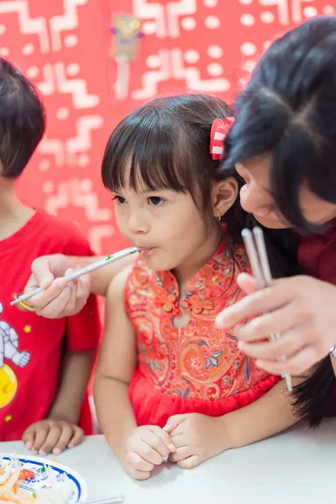 A woman is feeding a little girl with chopsticks.