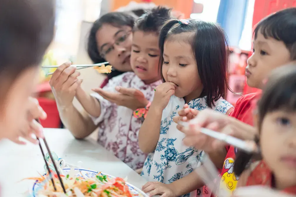 A group of children are sitting at a table eating food with chopsticks.