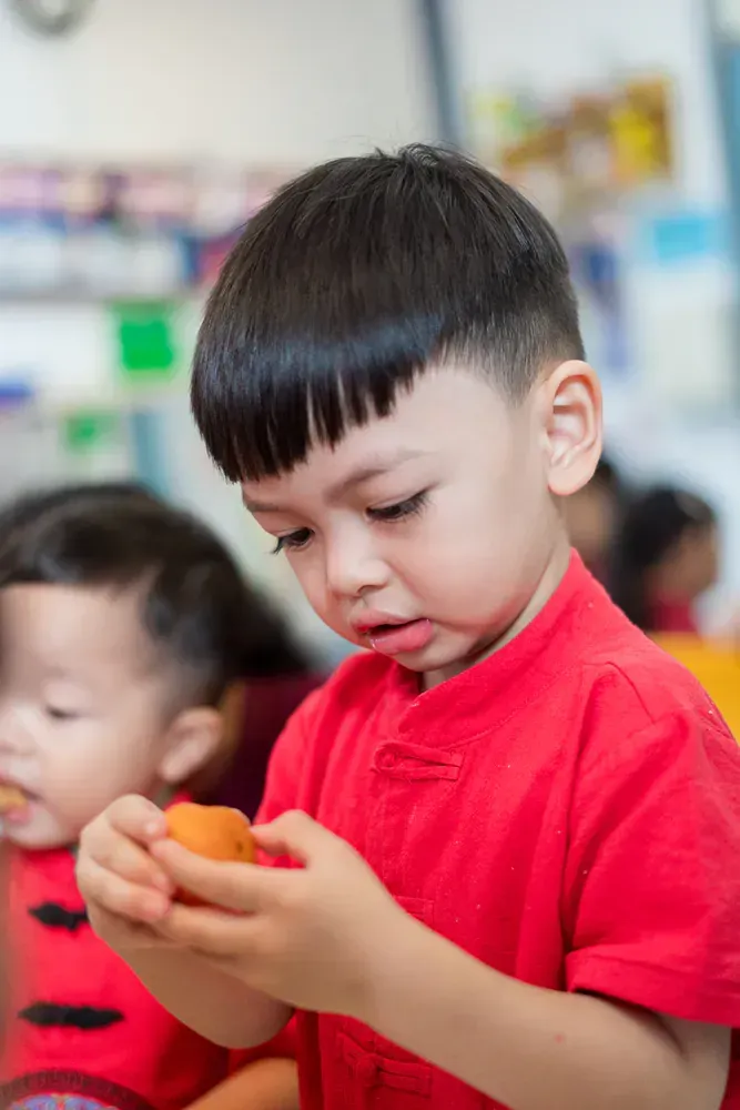 A young boy in a red shirt is holding an orange in his hands.