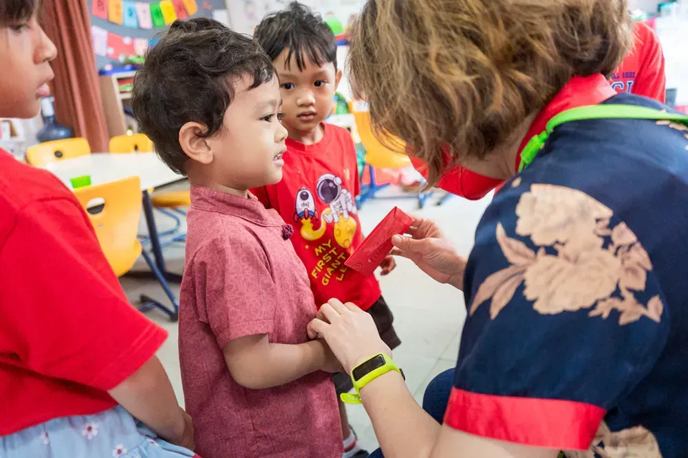 A woman is giving a red envelope to a young boy in a classroom.