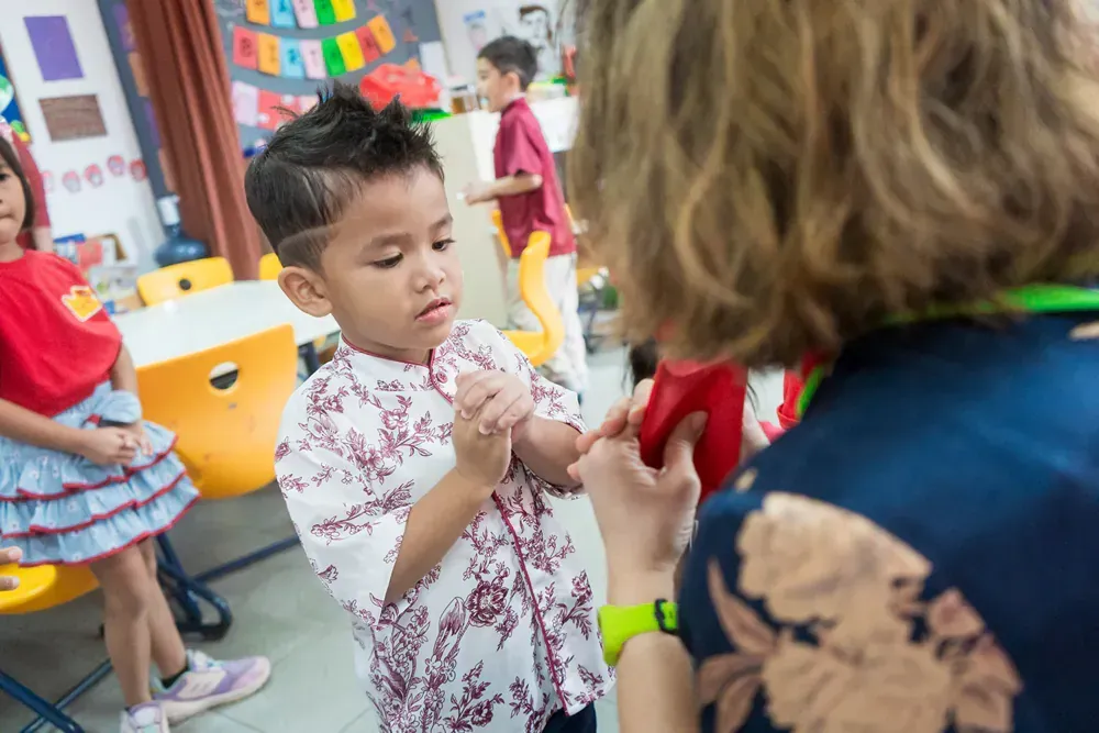 A woman is talking to a young boy in a classroom.