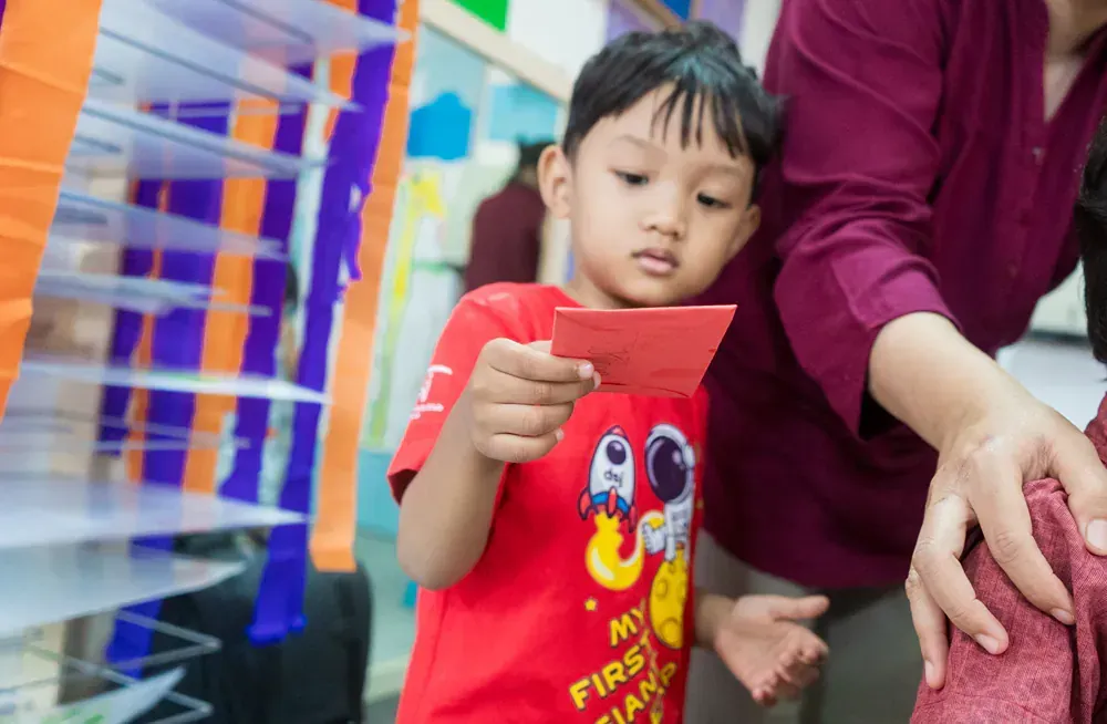 A little boy in a red shirt is holding a piece of paper in his hand.