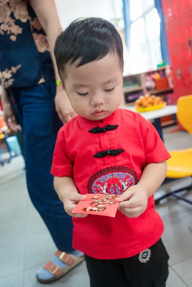 A little boy in a red shirt is holding a red envelope.