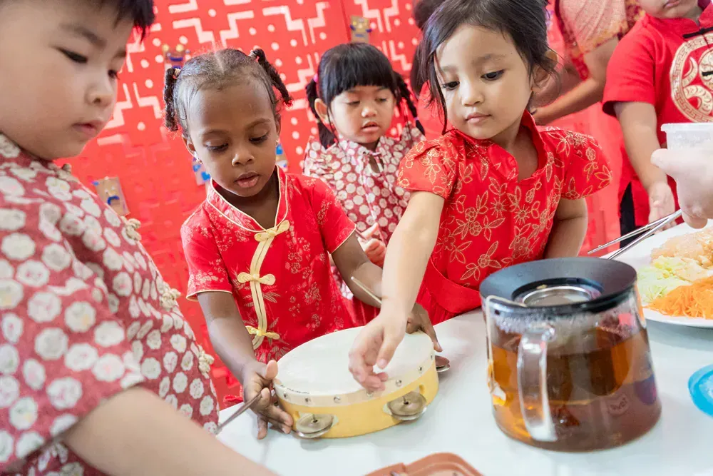 A group of children are playing a tambourine at a table.