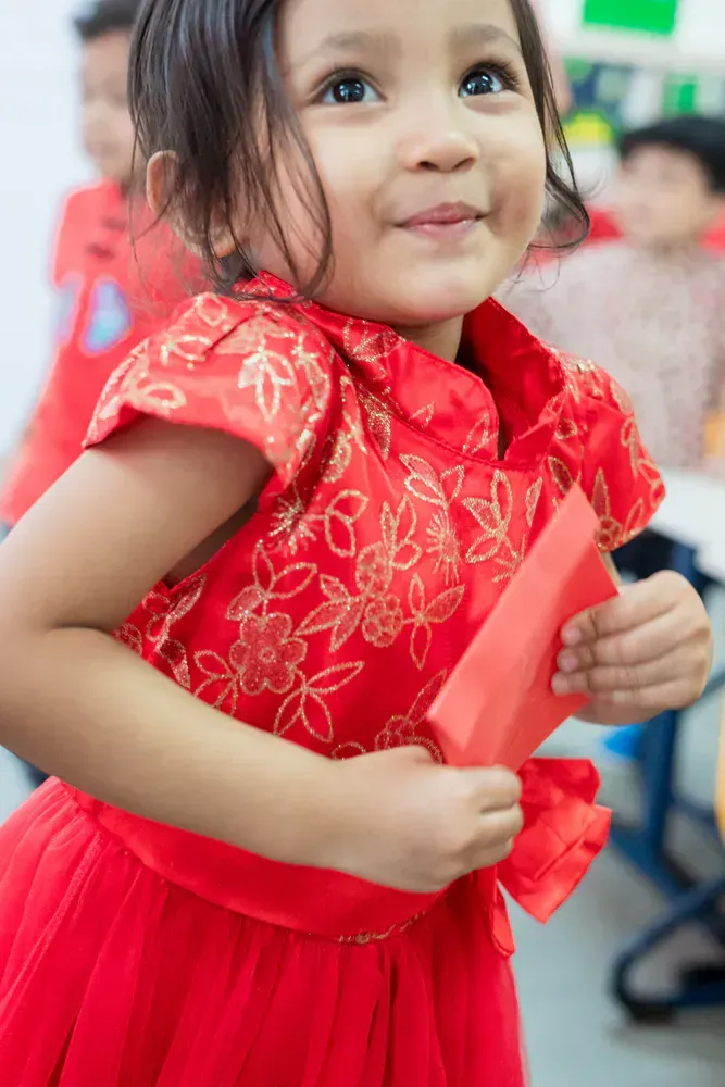 A little girl in a red dress is holding a piece of paper.