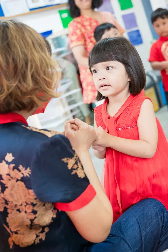 A woman is kneeling down next to a little girl in a red dress.