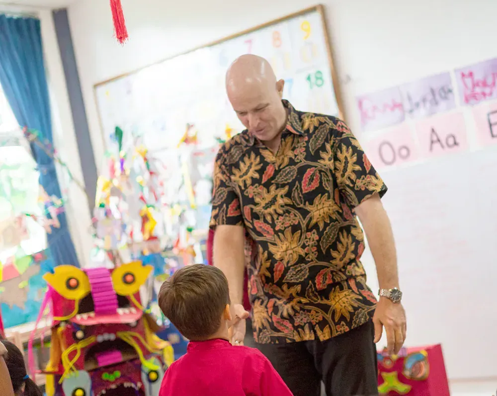 A man is talking to a young boy in a classroom.