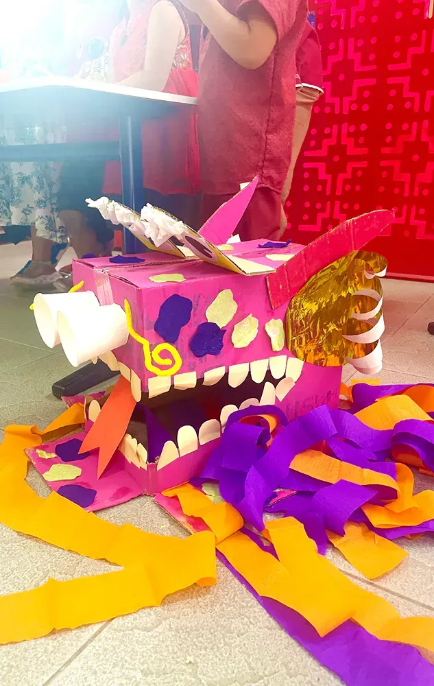 A pink dragon made out of cardboard is sitting on the floor.