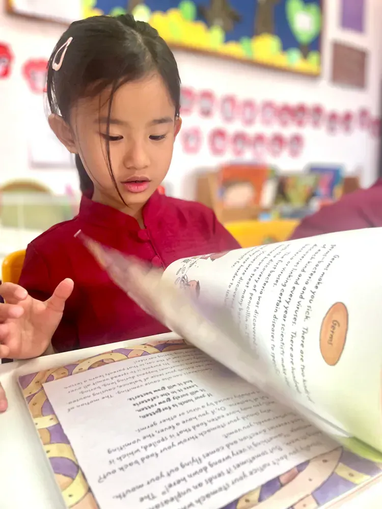 A little girl is reading a book in a classroom