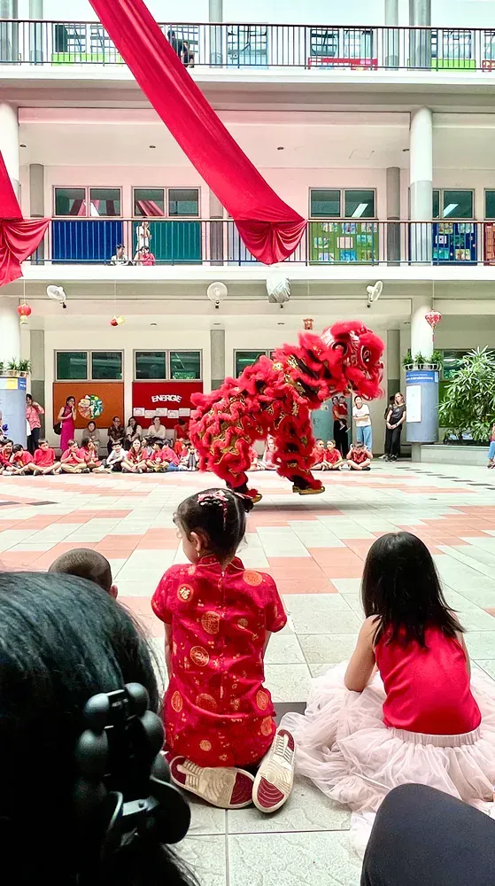 A group of children are watching a lion dance in a school.