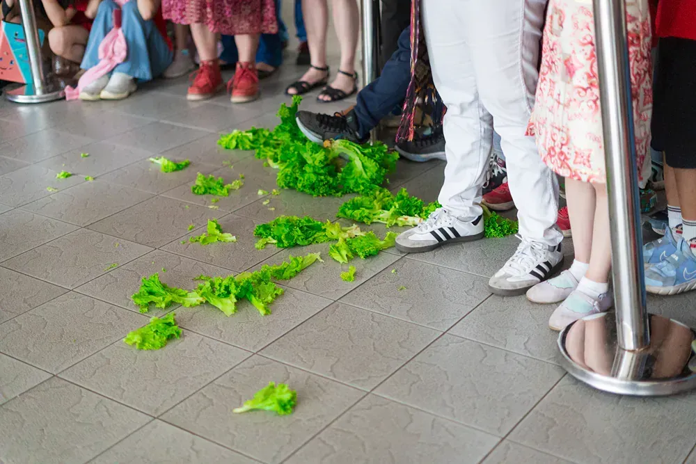 A group of people standing in a line with lettuce on the floor.
