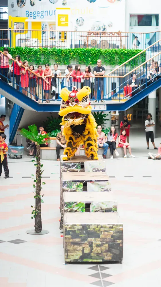 A lion is performing in front of a crowd of people in a mall.