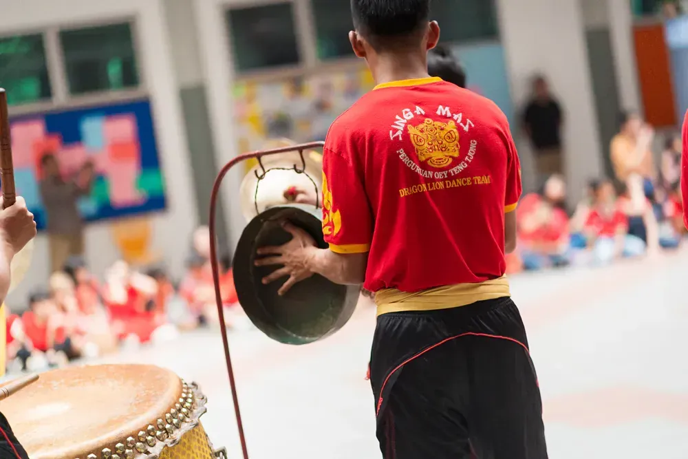 A man in a red shirt is playing a gong in front of a group of children.