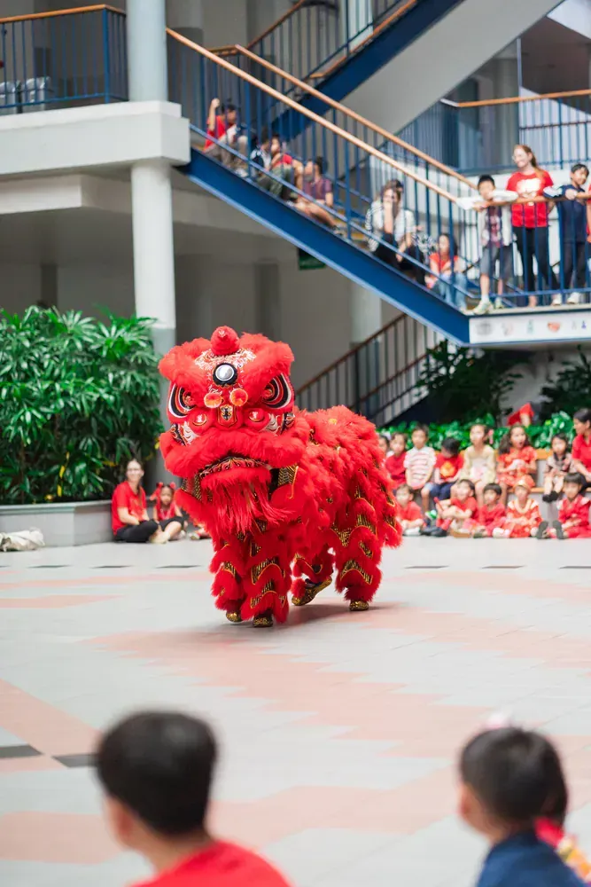 A red lion is dancing in front of a crowd of people.