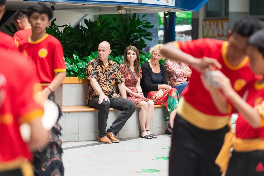 A group of people are sitting on a bench watching a group of people perform martial arts.
