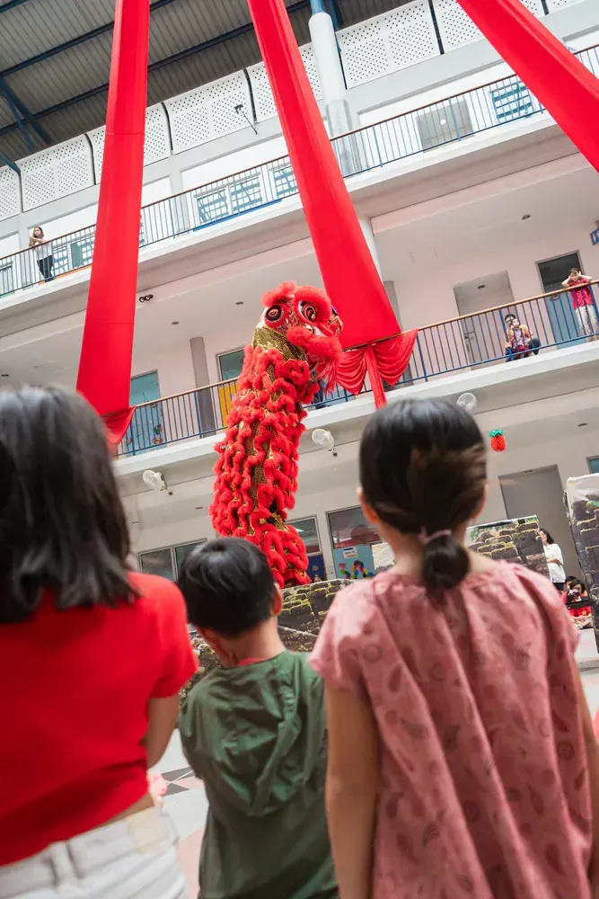 A group of children are watching a lion dance in a building.