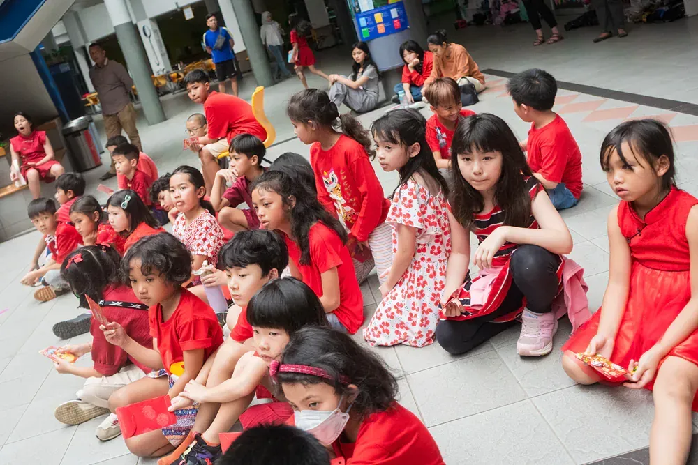A group of children in red shirts and dresses are sitting on the ground.