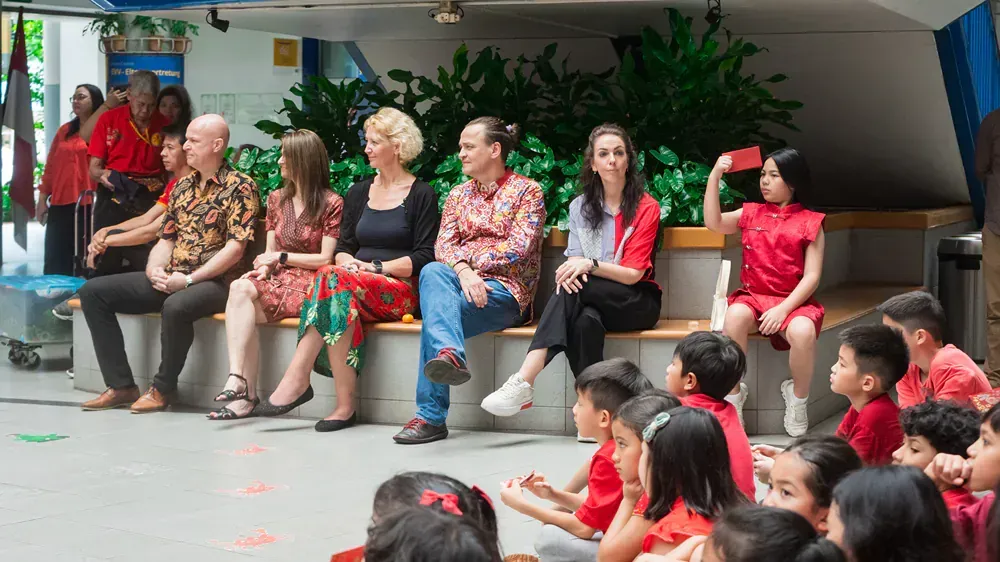 A group of people are sitting on a bench in front of a group of children.