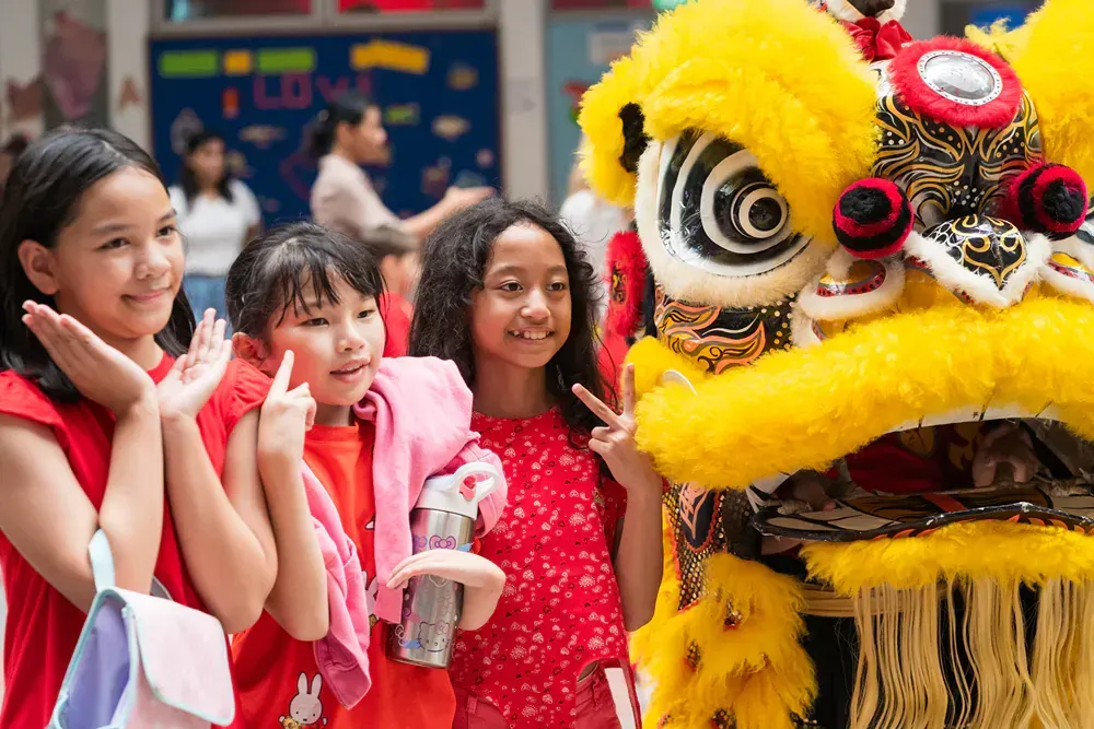 A group of young girls are posing for a picture in front of a lion costume.