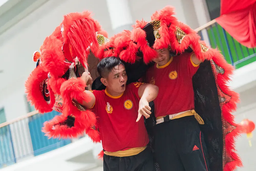 Two men are performing a lion dance in a building.
