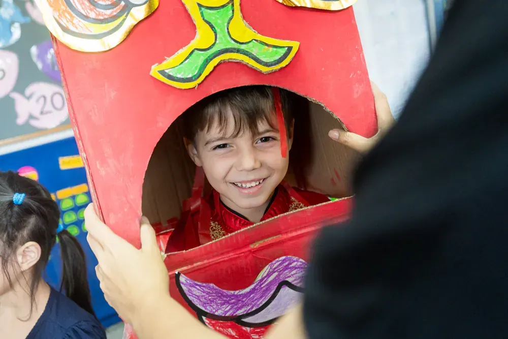 A young boy is looking out of a cardboard box.