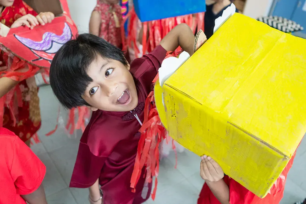 A young boy is holding a yellow box over his head.