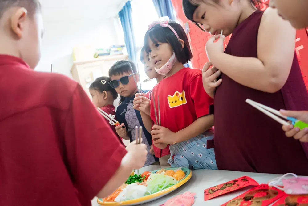 A group of children are standing around a table with chopsticks and a plate of food.