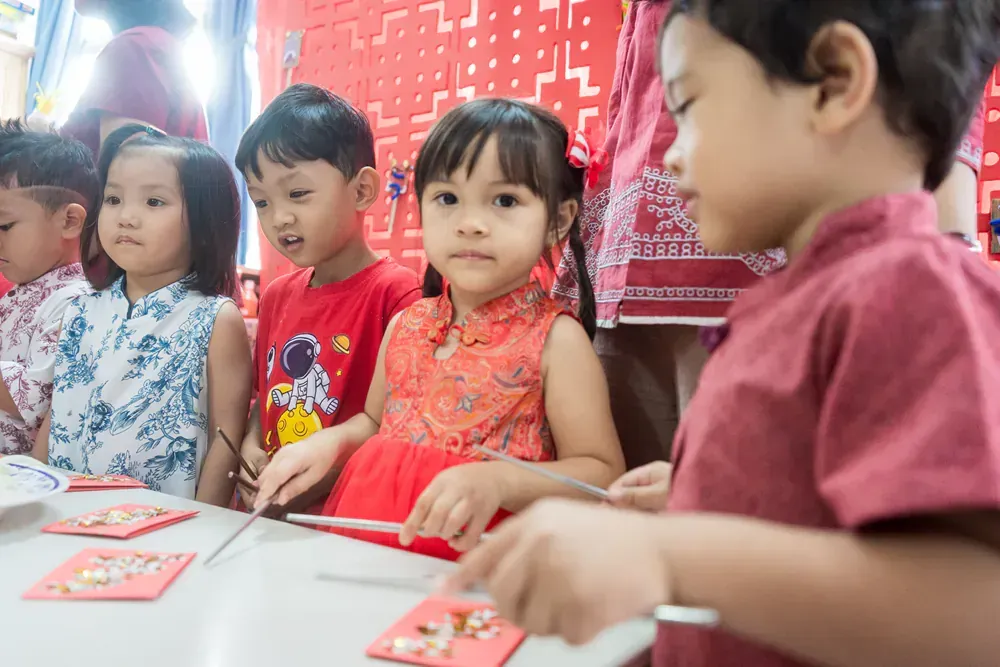 A group of children are sitting at a table cutting paper with scissors.